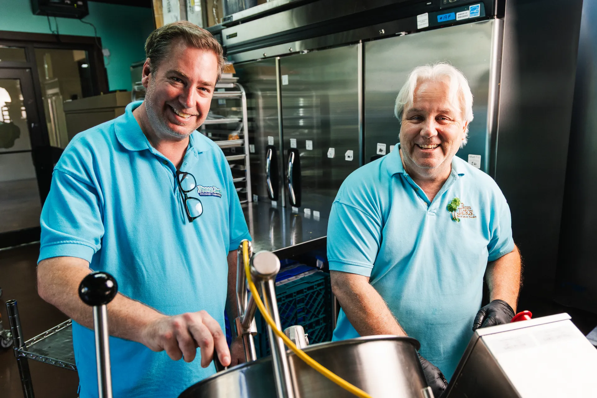 Two Pecan Jacks workers smiling beside candy-making equipment.